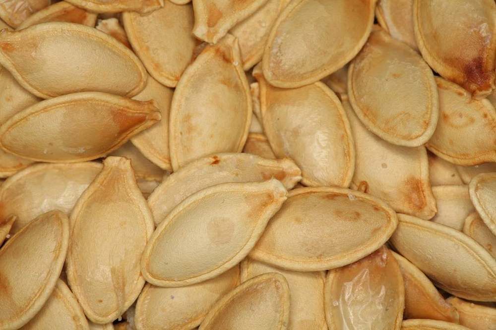 Pale pumpkin seeds, still in their shells, spread on a wooden board.