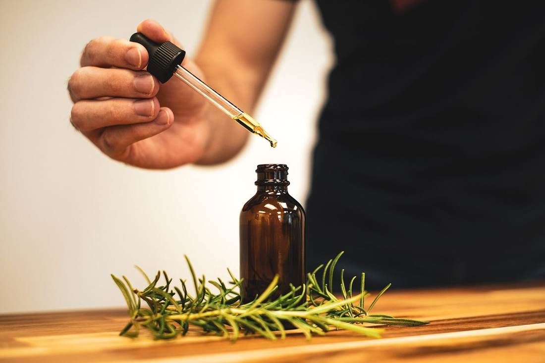 Rosemary oil poured from a glass bottle, with fresh rosemary sprigs beside it.